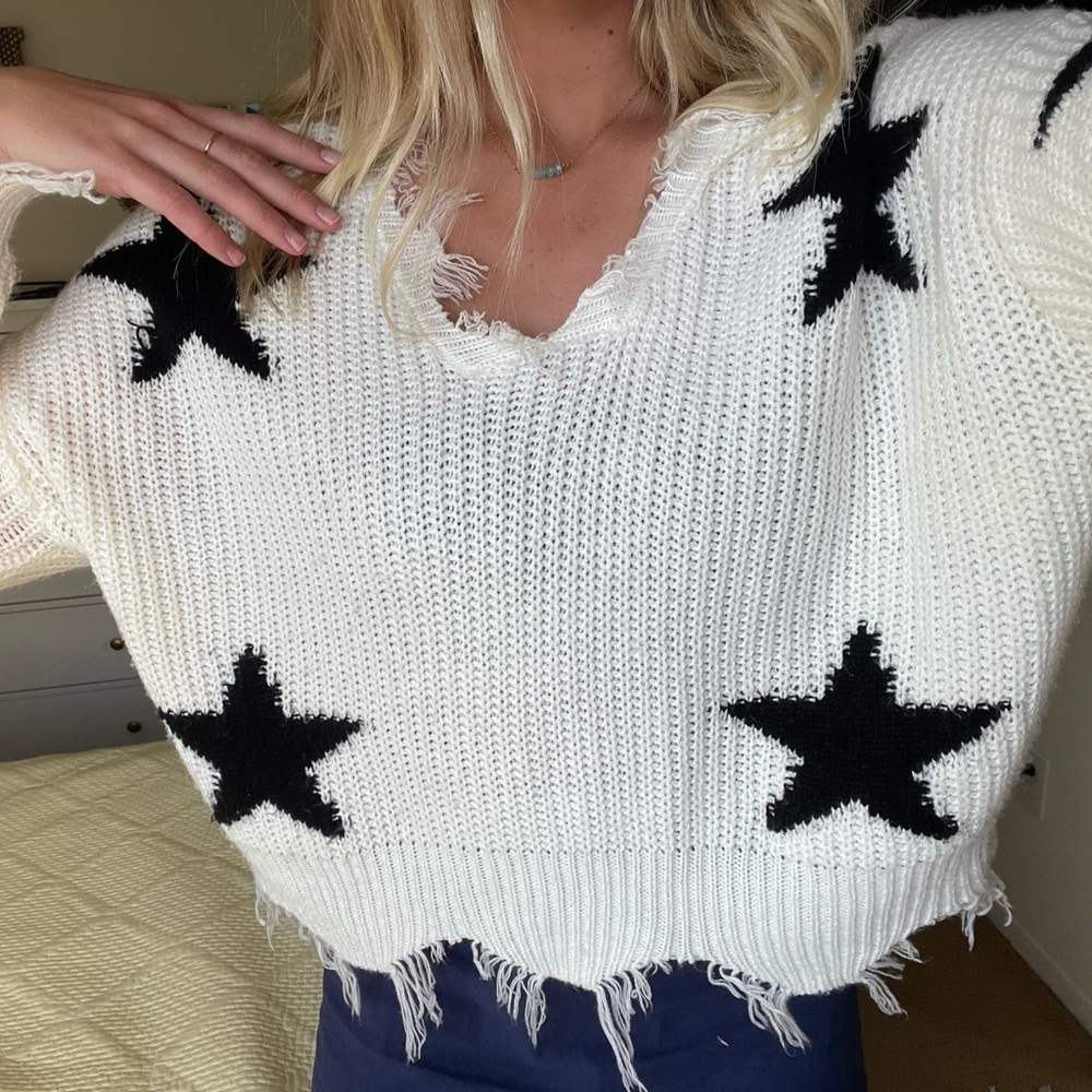 White sweater with black stars. Frayed sleeves.